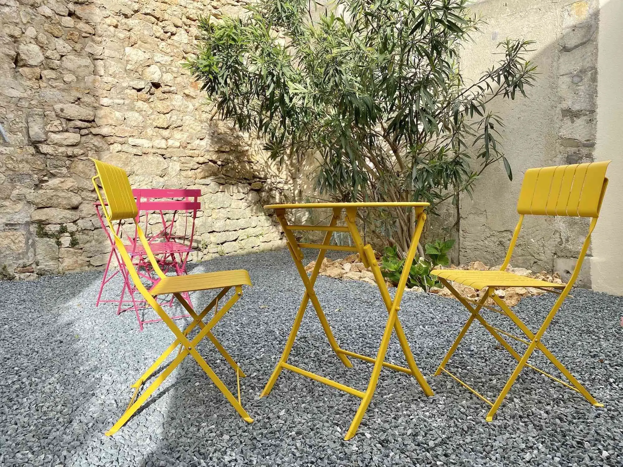 Cour intérieure arborée avec chaises colorées et mur en pierre